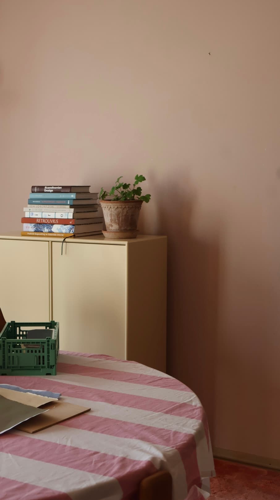 Gult skap med bøker og plante ved et bord med rosa stripete duk