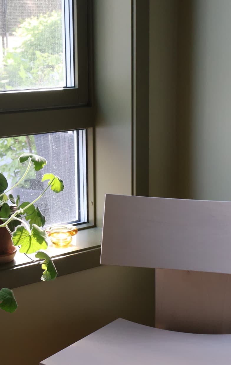 Lys trestol ved et grønt vindu med plante og gul glasskål