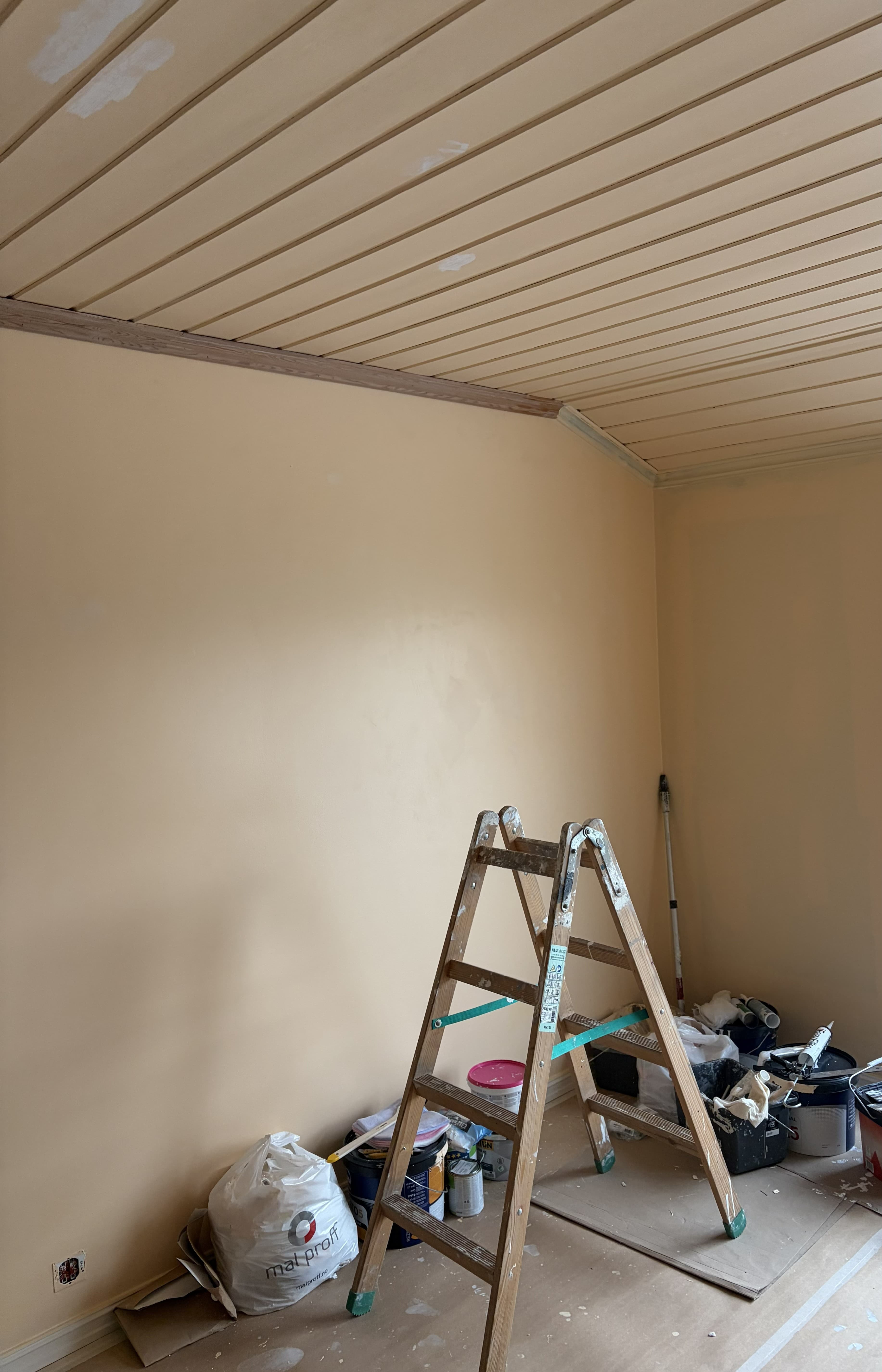 Rom under oppussing med beige vegger, paneltak og malerutstyr